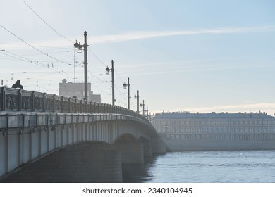 Automobile - pedestrian bridge over a large river in the old town with street lamps in the early morning in the fog, faded image.