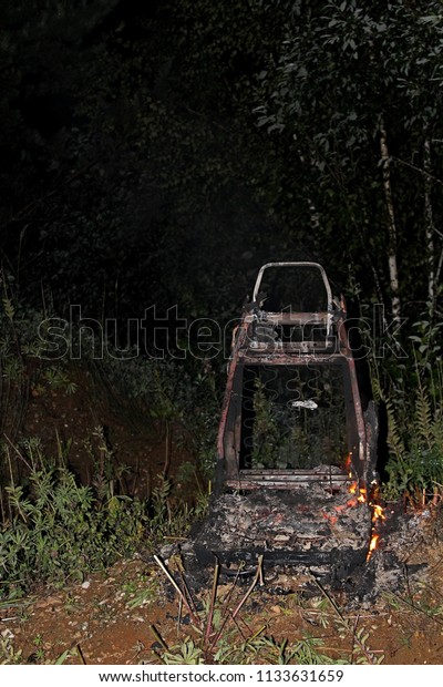 Automobile seat, covered in flames, in the open\
air, on a dark summer\
night.