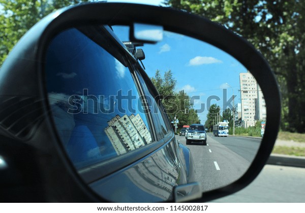 Automobile side view mirror\
and reflecting road with traveling cars, \
fuzzy outlines of a\
person inside