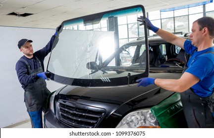Automobile special workers remove old windscreen or windshield of a car in auto service station garage. Background