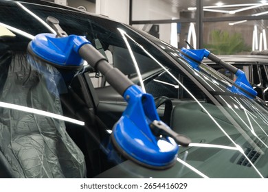 Automobile special workers replacing windscreen or windshield of a car in auto service station garage. Glass of the car, removed with the help of professional suction cups. The process of car repair. 