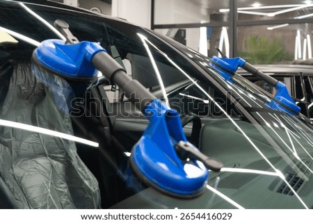 Automobile special workers replacing windscreen or windshield of a car in auto service station garage. Glass of the car, removed with the help of professional suction cups. The process of car repair. 
