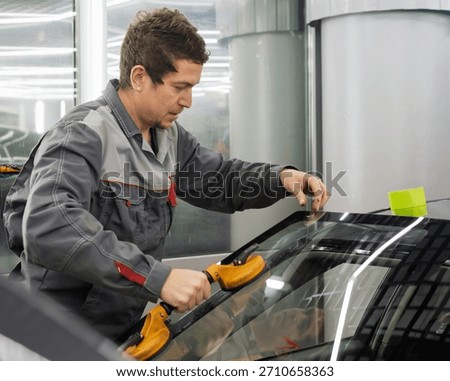 Automobile special workers replacing windscreen or windshield of a car in auto service station garage. Glass of the car, removed with the help of professional suction cups. The process of car repair. 