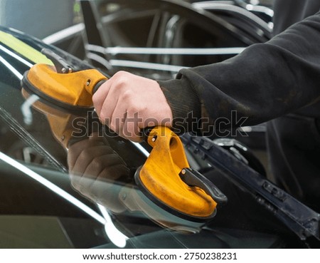 Automobile special workers replacing windscreen or windshield of a car in auto service station garage. Glass of the car, removed with the help of professional suction cups. The process of car repair. 