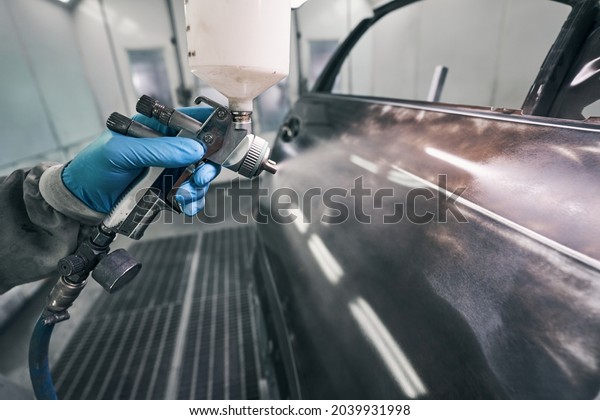 Automobile\
technician painting auto with spraying\
gun