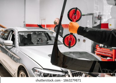 Automobile technician worker replacing windscreen or windshield of a car in auto service station garage. High quality photo