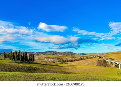  Automotive asphalt highway and motorway. Italy. Magnificent cypress alley. The magical beauty of the province of Tuscany. Sunny day at the beginning of winter. Huge sky over picturesque hills