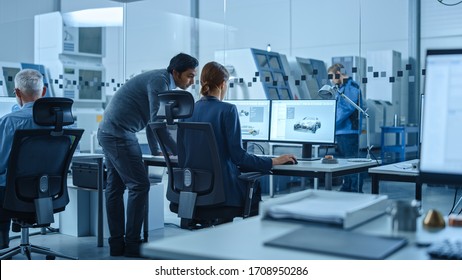 Automotive Design Factory: Project Manager And Chief Mechanical Engineer Talk, Point At Computer Display Showing 3D Electric Car Model In CAD Software. High Tech Facility With Automatic CNC Machinery