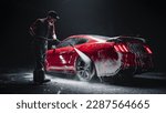 Automotive Detailer Washing Away Smart Soap and Foam with a Water High Pressure Washer. Red Performance Car Getting Care and Treatment at a Professional Vehicle Detailing Shop