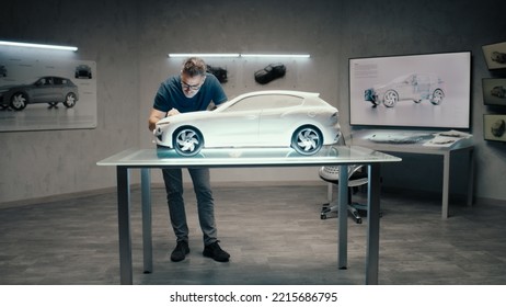 An Automotive Engineer And Designer Works On A Prototype Model Car In A Modern Studio With Bright LED Of An Automotive Company. Making Design Corrections.