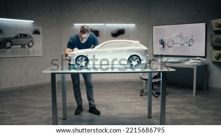 An automotive engineer and designer works on a prototype model car in a modern studio with bright LED of an automotive company. Making Design Corrections.