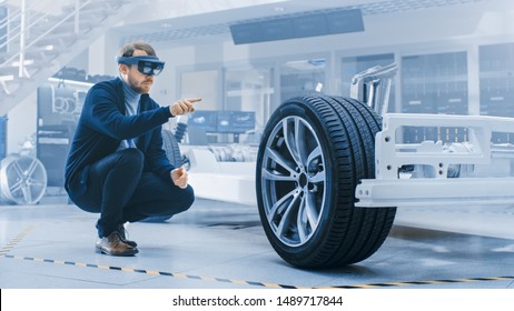 Automotive Engineer Working on Electric Car Chassis Platform, Using Augmented Reality Headset. In Innovation Laboratory Facility Concept Vehicle Frame Includes Wheels, Suspension, Engine and Battery.
