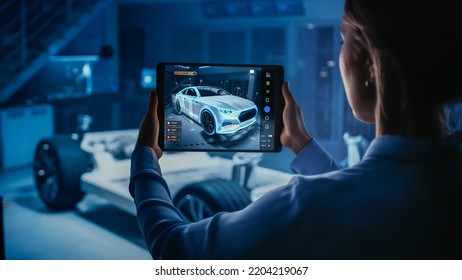 Automotive Engineer Working on Electric Car Chassis Platform, Using Tablet Computer with Augmented Reality 3D Software. Innovative Facility: Vehicle Frame with Wheels Becomes a VFX Model. - Shutterstock ID 2204219067