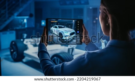 Automotive Engineer Working on Electric Car Chassis Platform, Using Tablet Computer with Augmented Reality 3D Software. Innovative Facility: Vehicle Frame with Wheels Becomes a VFX Model.