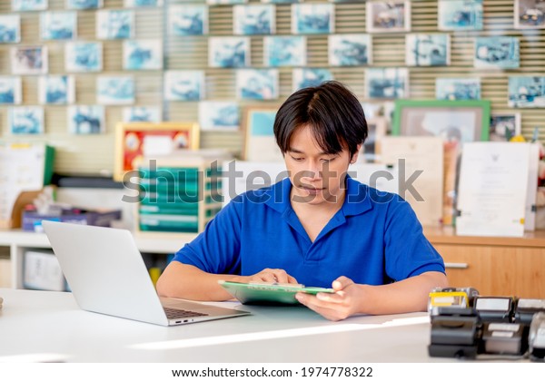 Automotive or garage worker with blue shirt uniform\
check list of document in the area of counter service and use\
laptop to support his\
work.