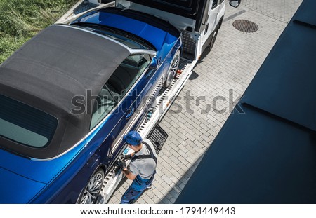 Automotive Industry Sales Theme. New Vehicle Home Delivery on a Towing Truck. Caucasian Driver Removing Safety Belts to Release the Car.