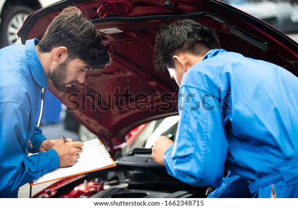automotive mechanic men with team assistant\
checking damage part under car condition, vehicle maintenance\
technician write on checklist document in garage at auto repair\
shop. after service\
concept