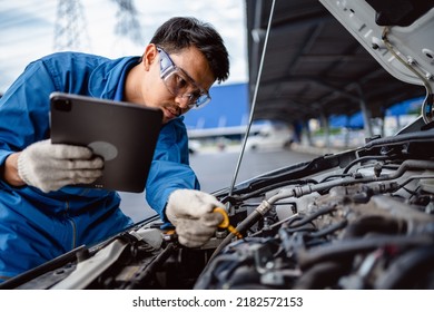 Automotive mechanic repairman using tablet and pulling dipstick to checking engine oil level engine in the engine room, check the mileage of the car, oil change, auto maintenance service concept. - Powered by Shutterstock