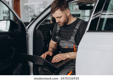 Automotive mechanic running diagnostics software on computer. Mechanic sitting in car and working on laptop while doing vehicle diagnostic test in auto service garage. - Powered by Shutterstock