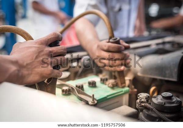Automotive mechanic uses battery jumper cables\
for chargers and jump starters a dead battery, maintenance car\
battery concept.