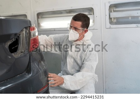 Automotive paint services, quality auto body shop concept. Male car mechanic inspecting quality auto body in automotive paint service shop. Technician checking, cleaning before painting car frame body