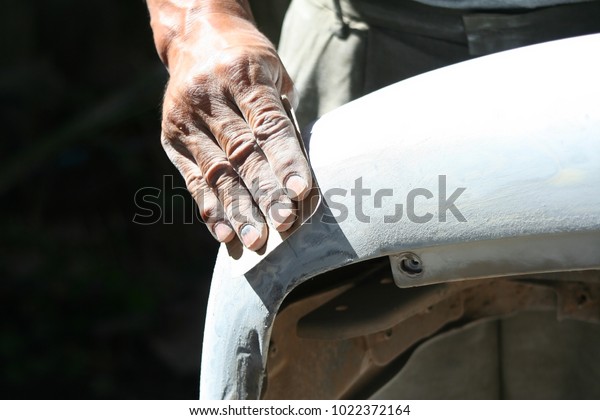 Automotive paint\
technician using grinder paper on car bumper,As part of the\
procedure to paint a new bumper\
car.