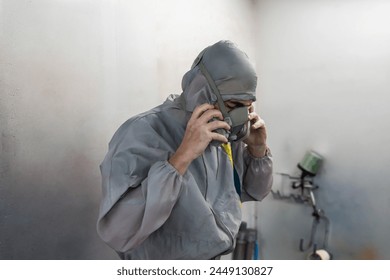 An automotive painter adjusts his respirator mask in a workshop, ensuring safety before starting a paint job. - Powered by Shutterstock