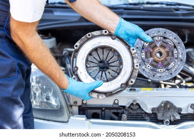 Automotive Technician Holding Used Car Pressure Plate And Clutch Disc In Front Of The Vehicle Engine