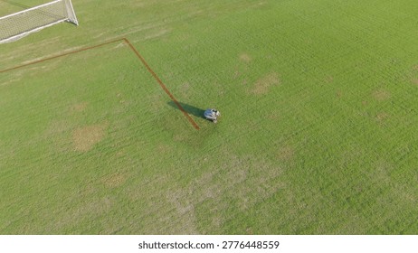 An autonomous machine marks boundaries on a green sports field during a bright sunny day.