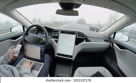 AUTONOMOUS TESLA CAR, FEBRUARY 2016: Self-driving Tesla Model S car autopilot demanding driver attention to hold steering wheel & take control on highway. Man working on laptop & texting on mobile