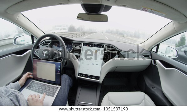 AUTONOMOUS\
TESLA CAR, FEBRUARY 2016: Luxury Tesla Model S autonomous automated\
electric car self-driving on freeway in the morning. Unrecognizable\
businessman working on laptop while\
traveling