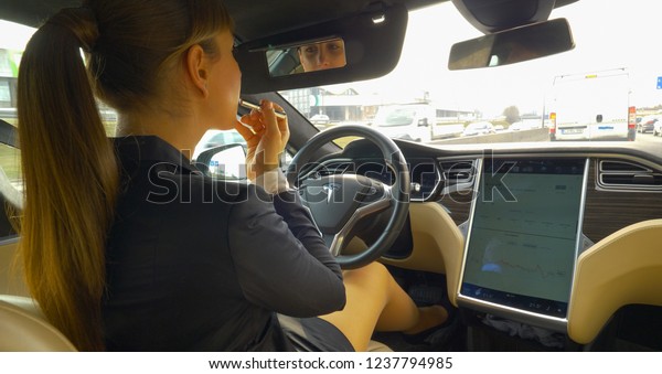 AUTONOMOUS TESLA CAR, MARCH 2018 - CLOSE UP:\
Young businesswoman getting ready while autonomous car drives her\
to work down the busy highway. Caucasian girl putting lip gloss on\
before job\
interview.