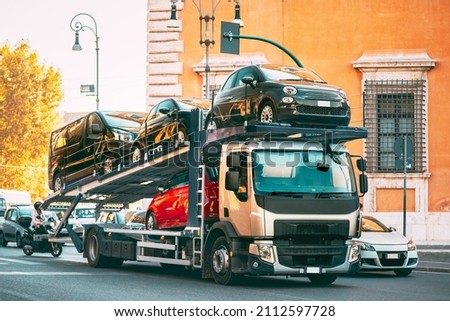 Auto-transport Carrying New Fiat Cars In European City Street. Auto Transport Broker Or Car Transporter. Auto-transport Carrying New Fiat Cars In City Street. Auto Transport Broker Or Car Transporter