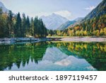 Autumn alps mountains in day light reflected in calm waters of green lake Jasna, Kranjska Gora. Slovenia. 