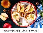 Autumn Apple Brie Crostini with Walnuts and Honey, Fall dinner, Thanksgiving party appetizers idea. Small sandwiches with red apple slices, brie cheese and sweet honey drizzles