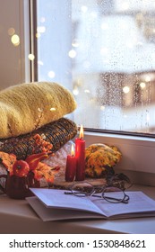 Autumn background by the window with a book and glasses, warm winter things and autumn flowers, beautifully burning red candles in the center of the composition.  Rainy evening. - Shutterstock ID 1530848621
