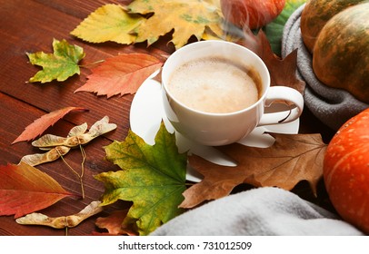 autumn background with a cup of hot aromatic coffee on a wooden table surrounded by autumn leaves and a rug