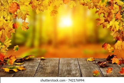 Autumn background with falling leaves and empty wooden table,  ideal for product placement or free space for text. Seasonal abstract vivid colored background
