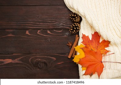 Autumn background. Knitted sweater, autumn leaves , cones and cinnamon sticks on brown wooden board. - Powered by Shutterstock