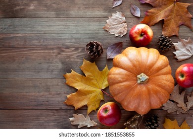 Autumn background with ripe orange pumpkin, red apples, pine cones and dry fallen leaves on rustic wooden table. Happy Thanksgiving day, fall and harvesting concept. Flat lay, top view, copy space. - Powered by Shutterstock