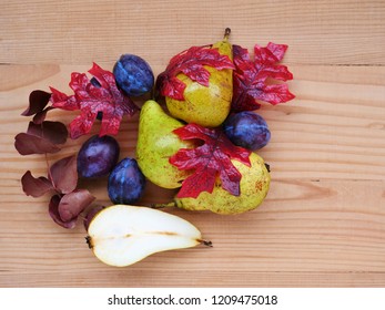 Autumn background with seasonal fruits, pears, plums and fall leaves over wooden table