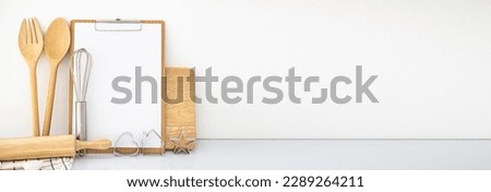 Autumn baking background, baking utensils, cookies, pie, rolling pin, whisk, wooden fork spoon, chopping board on white table Front view copy space, with notebook menu board for recipes banner