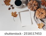 Autumn breakfast concept. Blank greeting card mockup, envelope. Cup of coffee, colorful maple leaves, acorns and orange pumpkins. White table background, Thanksgiving, Halloween concept, flatlay, top