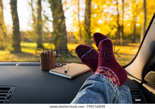 Autumn car trip. Woman feet in warm wool\
socks and cup of tea in the car. Freedom\
concept