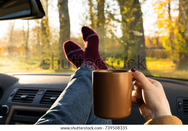 Autumn car trip. Woman in warm wool socks and cup of\
tea in the car