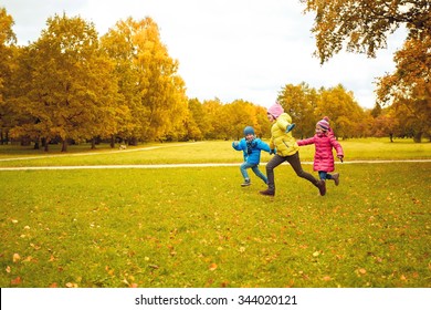 Autumn, Childhood, Leisure And People Concept - Group Of Happy Little Kids Playing Tag Game And Running In Park Outdoors