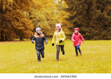 Autumn, Childhood, Leisure And People Concept - Group Of Happy Little Kids Playing Tag Game And Running In Park Outdoors