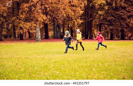 Autumn, Childhood, Leisure And People Concept - Group Of Happy Little Kids Playing Tag Game And Running In Park Outdoors