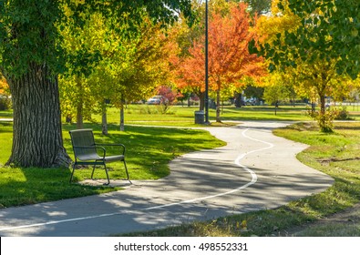 Autumn City Park - A Sunny Autumn Afternoon View Of A Quiet Running Trail Winding In A City Park, Denver/Lakewood, Colorado, USA. The Focus Is On The Iron Bench.