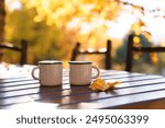 Autumn coffee picnic in garden. Camping cups on wooden table in fall forest. Hot drinks in slow travel outdoor. Vacation in Indian summer. Herbal tea and pumpkin spice latte in reusable mug at nature